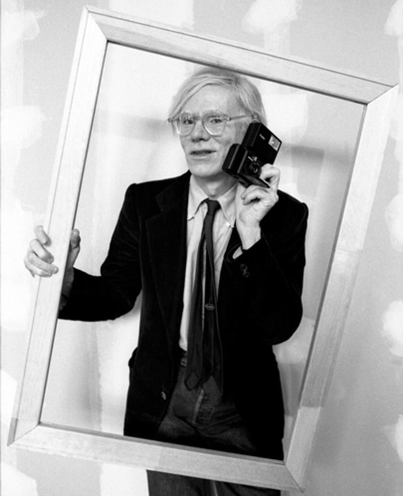 Andy Warhol posing with camera and a picture frame