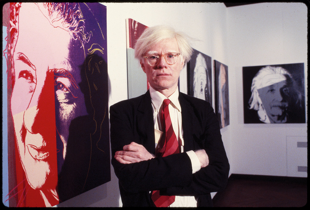 Andy Warhol standing with screen prints from his Ten Famous Jews of the Twentieth Century series.