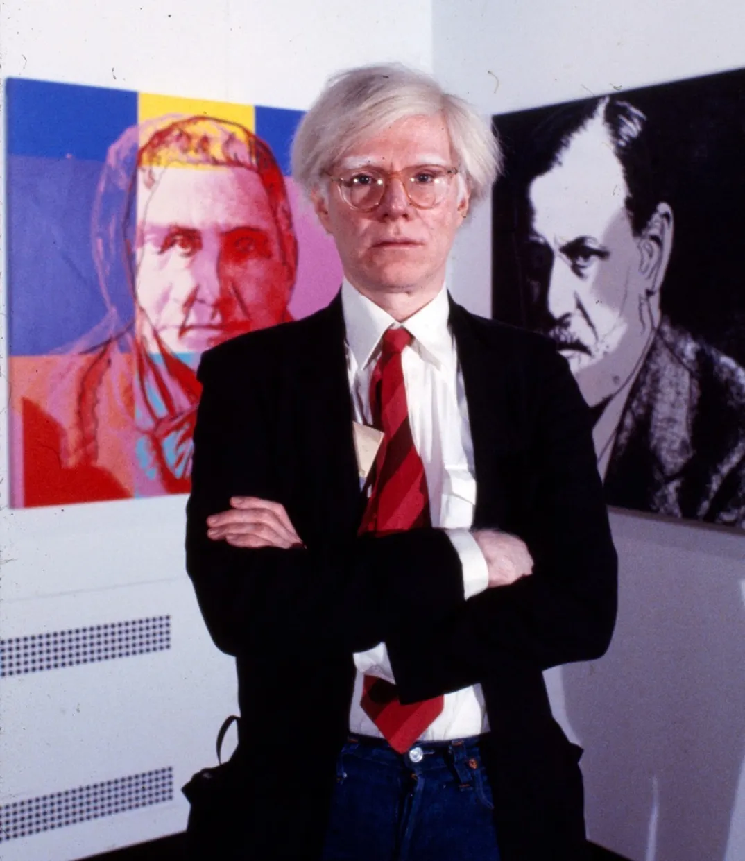 Warhol standing in front of his prints of Sigmund Freud and Gertrude Stein.