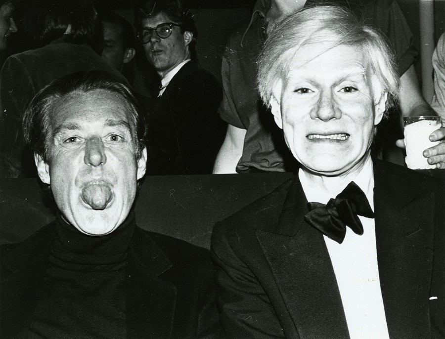 Warhol and Halston sitting side by side making funny faces at the camera.
