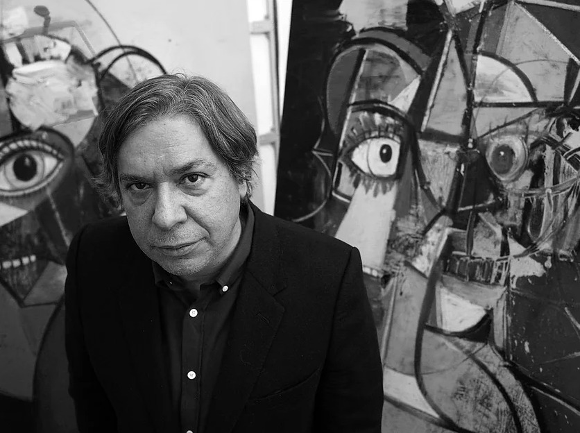 Portrait of George Condo with his paintings in the background.