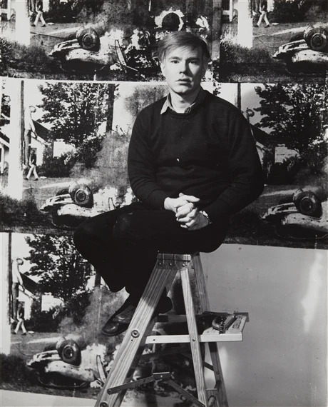 Andy Warhol sitting in front of one of his Death and Disaster paintings.