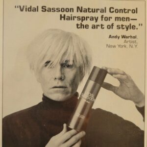 Andy Warhol wears a wig and holds a bottle of hair spray for men in a magazine advertisement.