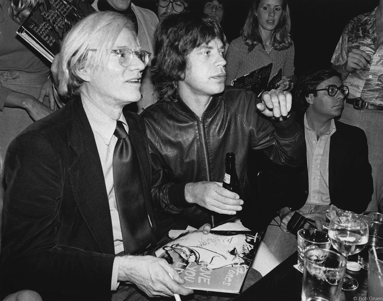 Andy Warhol and Mick Jagger sitting on a couch.