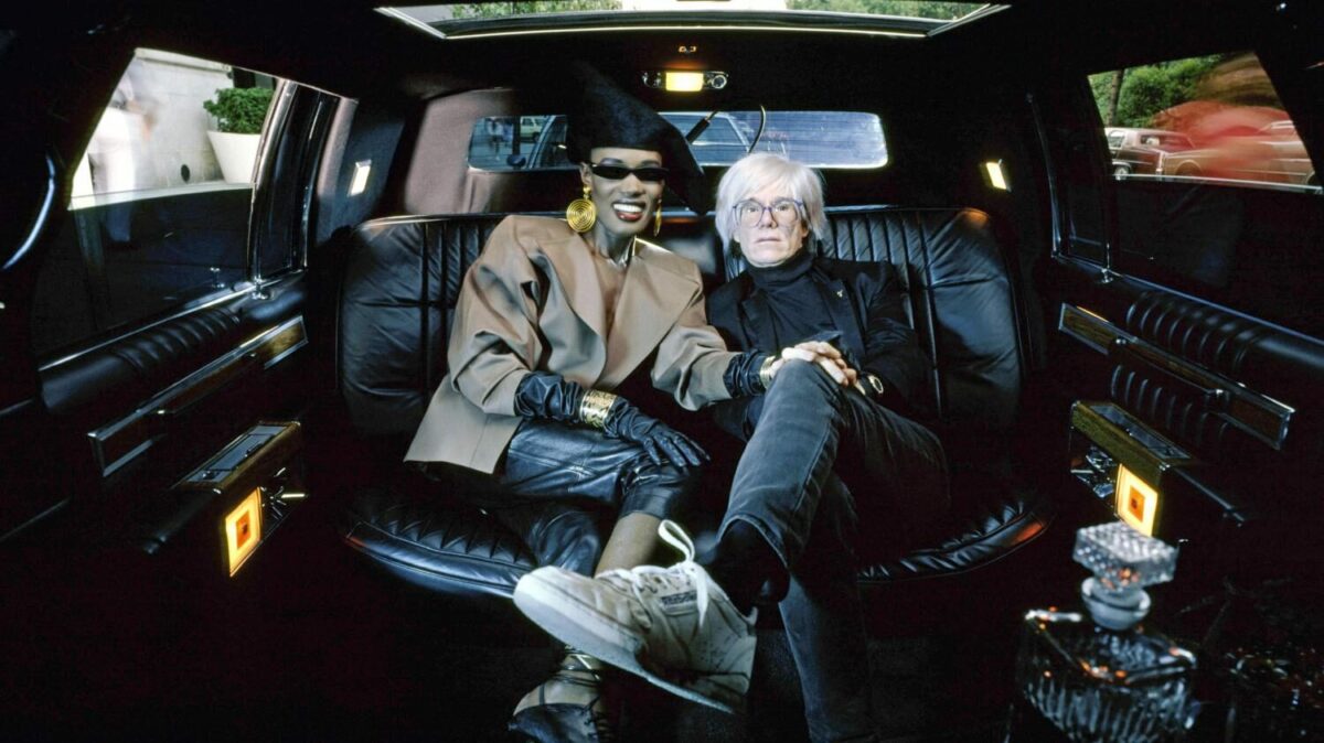 Grade Jones and Warhol sitting together in the back of a car.