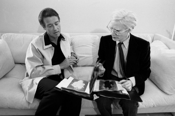 Fashion Designer Halston and Andy Warhol sitting on a couch together.